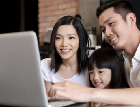 Picture of a family of three sitting in front of a laptop smiling